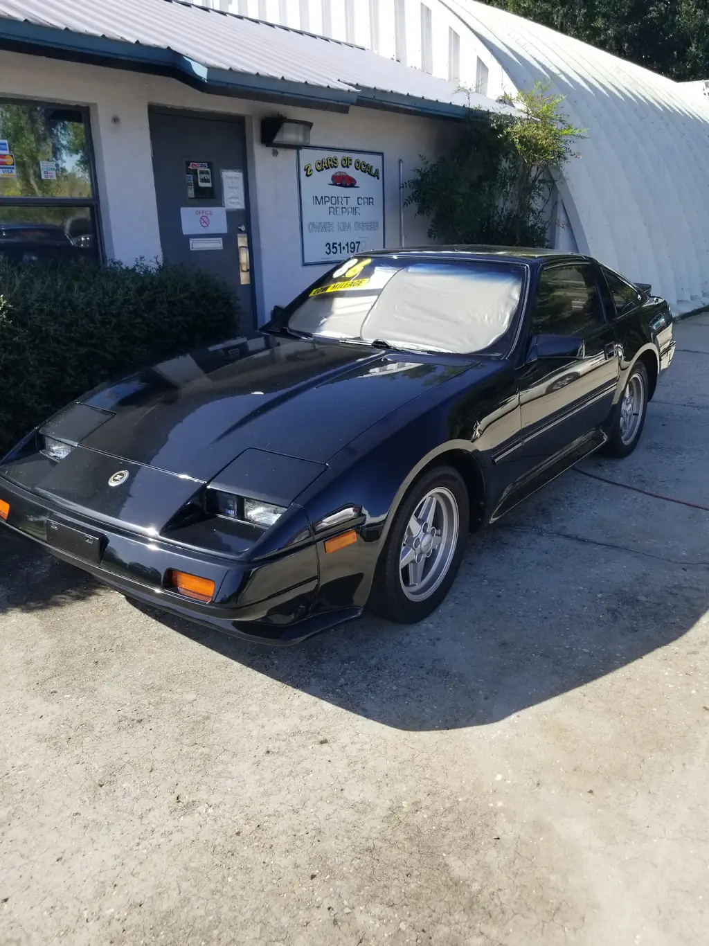 Black Nissan 300ZX parked under the hand-painted Z Cars of Ocala sign