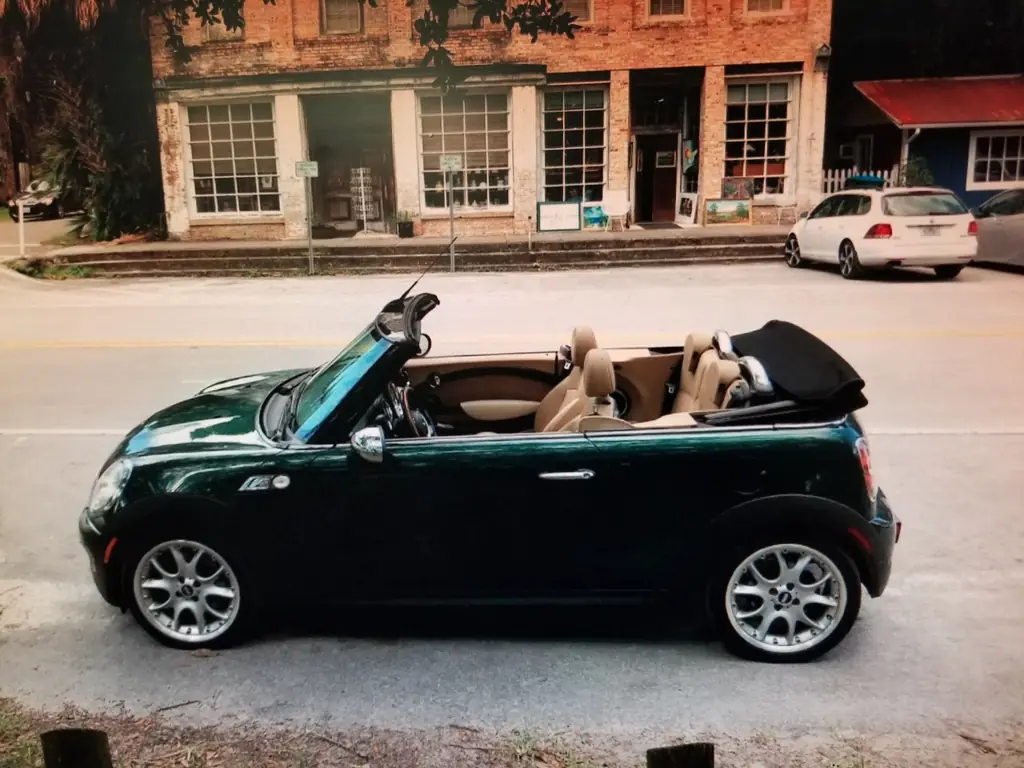 British racing green Mini Cooper S convertible outside a historic brick storefront